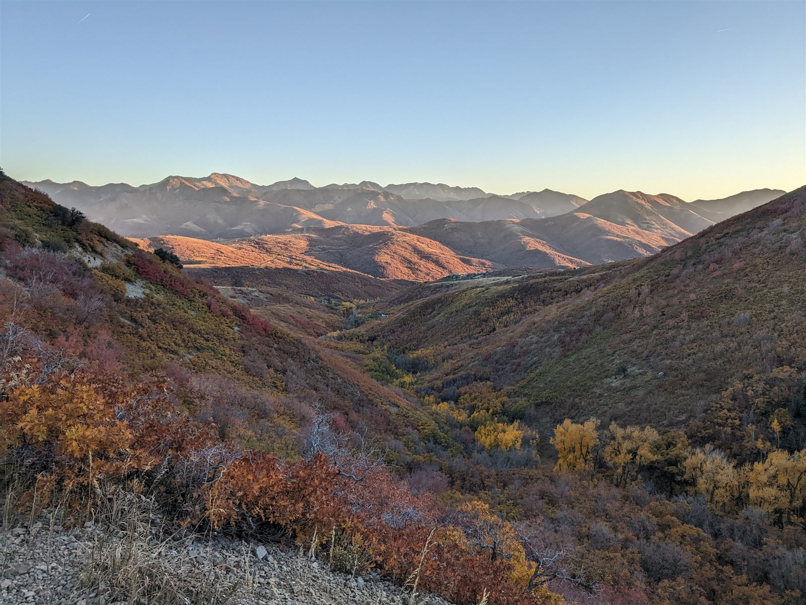 Golden-hour view down a Wasatch Back valley with hikers visible on a distant ridge trail